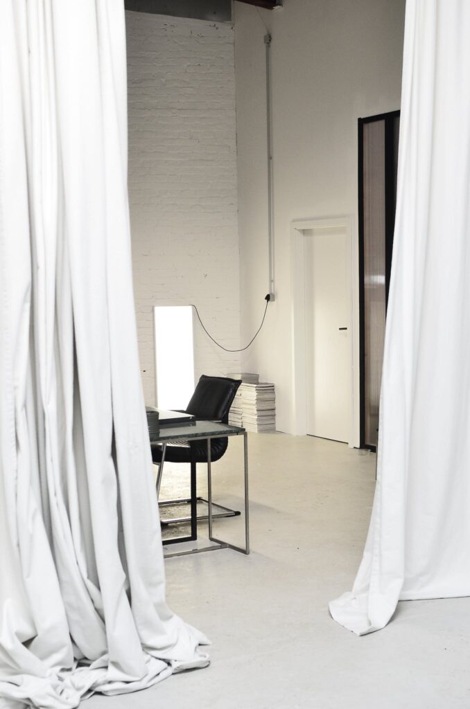 Interior of spacious loft studio with meeting table and chairs surrounded by hanging white curtains